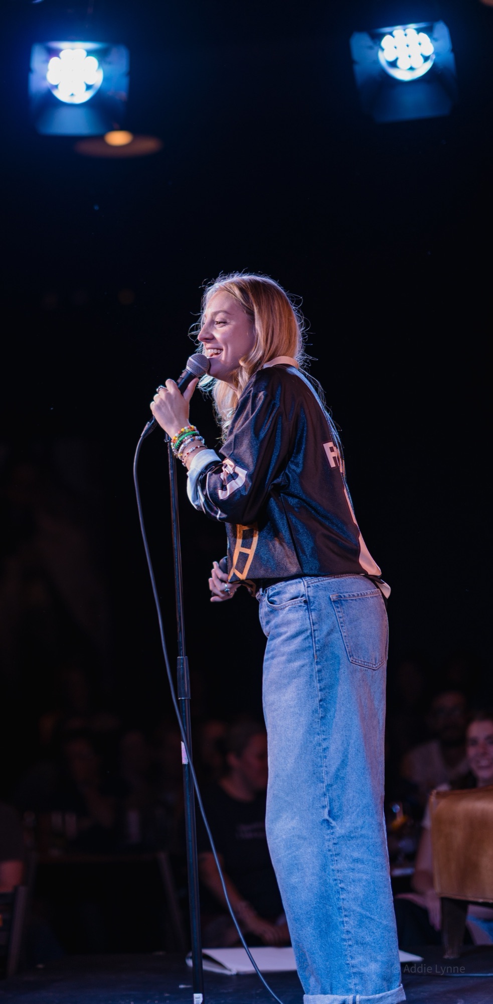 Madison Walser laughing into the microphone on stage at a stand-up show