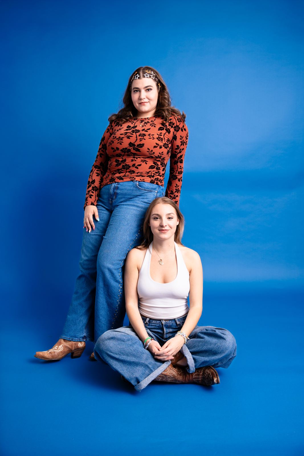 Erin standing and Madison sitting cross-legged in front of a blue backdrop