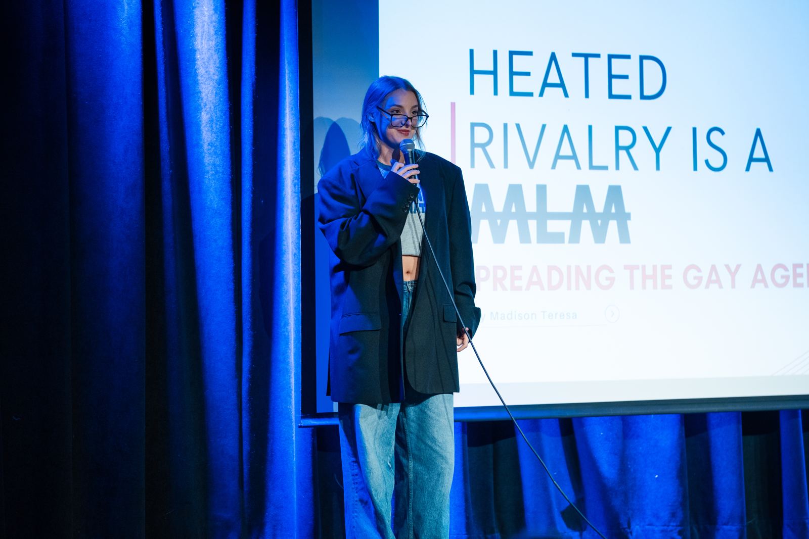 Madison on stage in front of a slide that reads Heated Rivalry is a MLM